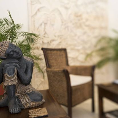 The photo depicts a serene studio space featuring a Buddha statue and rattan furniture, suggesting a focus on relaxation or mindful movement.
