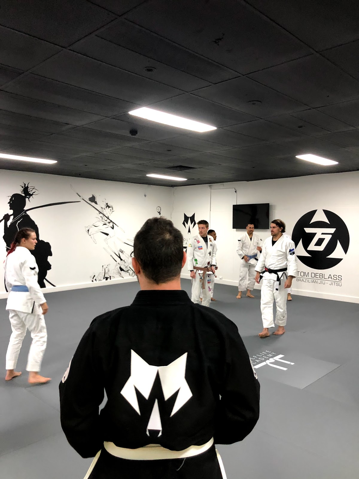 A group of people are practicing Jiu-Jitsu on mats in a dimly lit gym with an industrial feel.