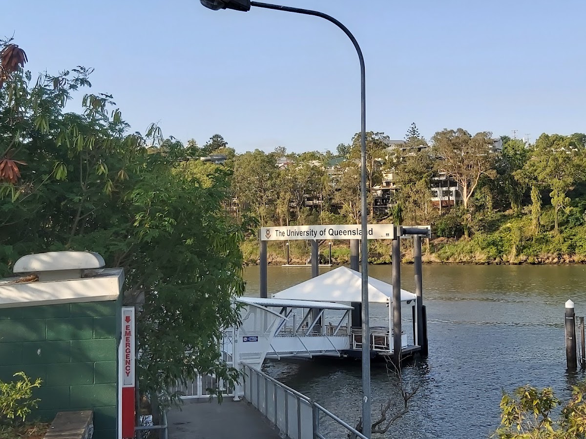 This photo shows an exterior view of a building near a river with a dock and greenery in the background.