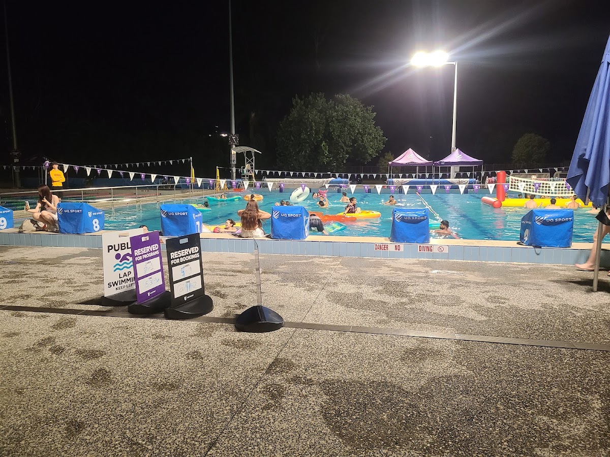 An outdoor swimming pool with lanes marked for lap swim, illuminated at night, and featuring signage indicating reserved areas.