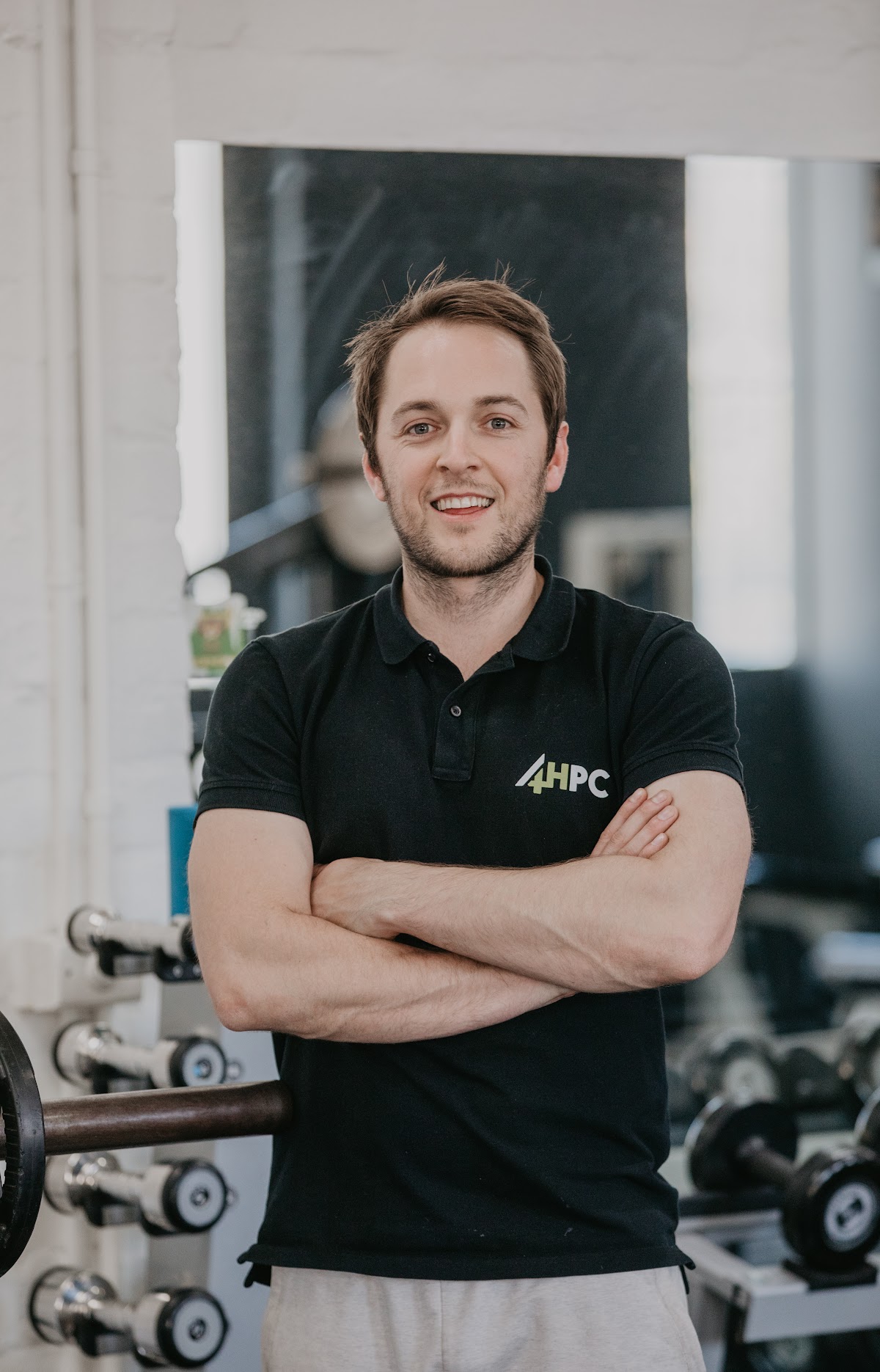 A portrait of a male trainer standing confidently in front of gym equipment.