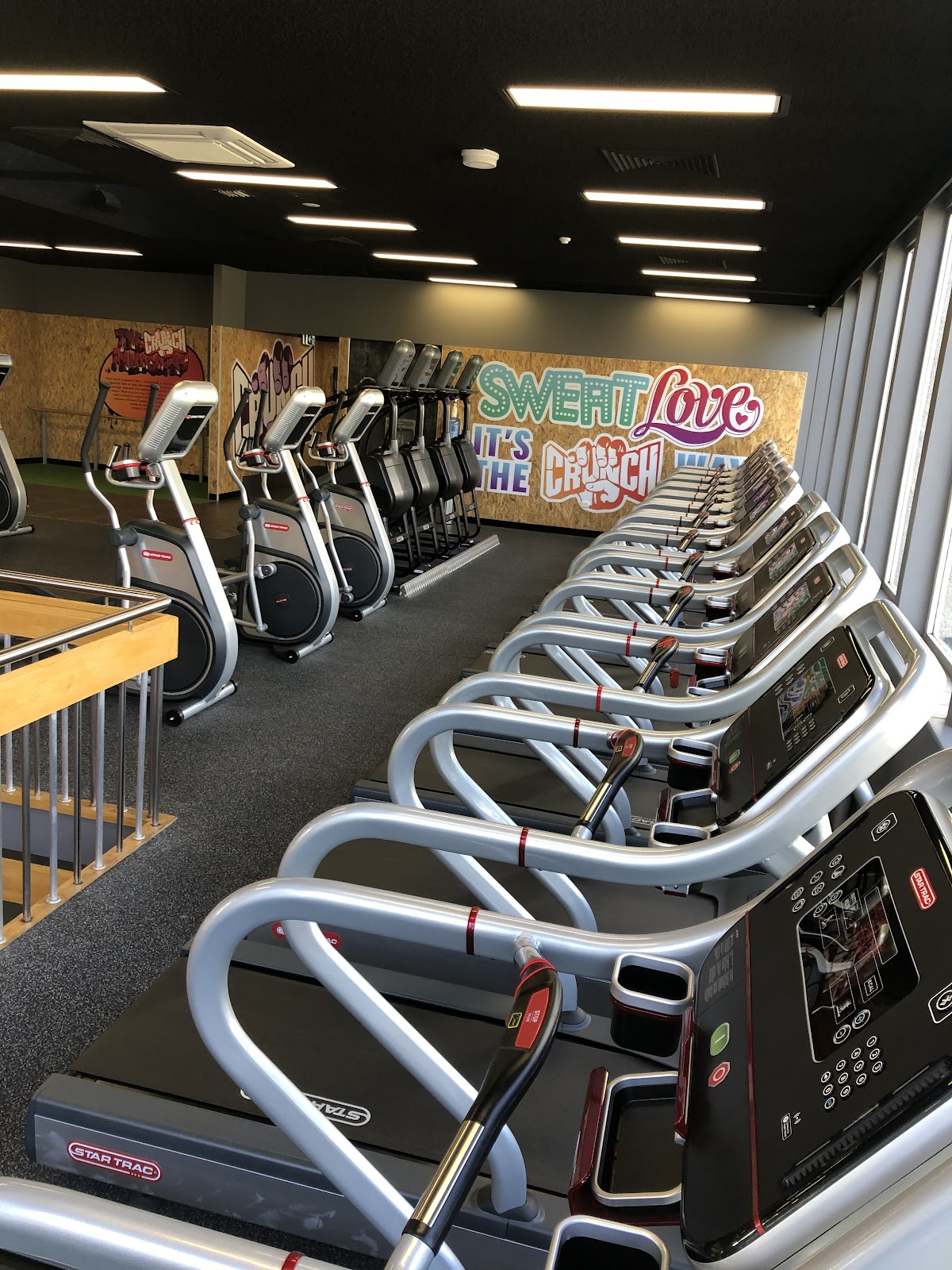 A row of treadmills lines the floor of a brightly lit gym with motivational signage on the wall.