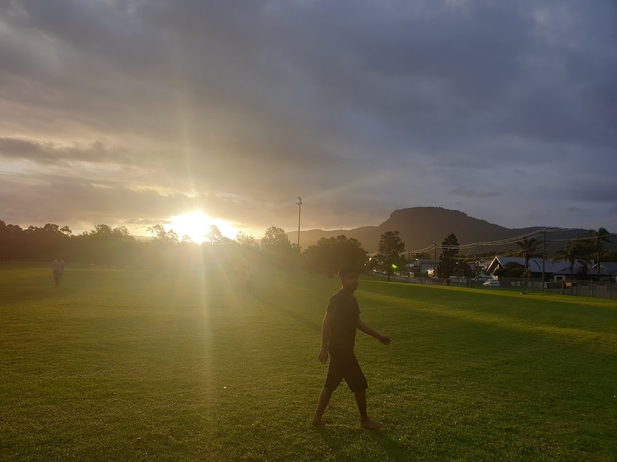 A person is walking across a grassy field during sunset with another person visible in the distance.
