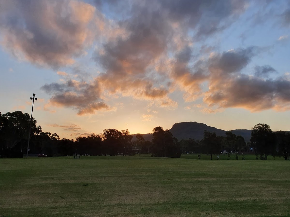 A scenic outdoor training area with a grassy field and mountains in the background under a dramatic sunset sky.