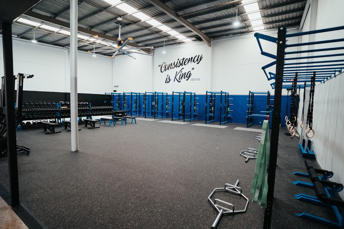 This photo showcases a large gym space with powerlifting equipment like squat racks and benches, featuring a motivational quote on the wall.