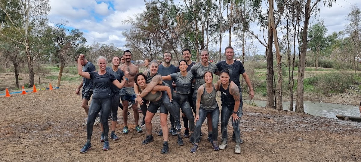 A group of people covered in mud pose for a photo after an outdoor fitness bootcamp event.