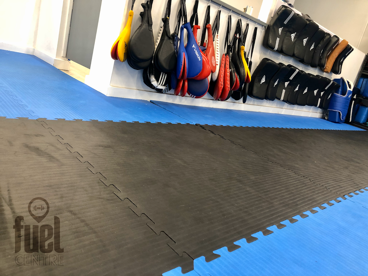 The photo shows a gym floor with boxing bags and mats, likely for martial arts or fitness training.