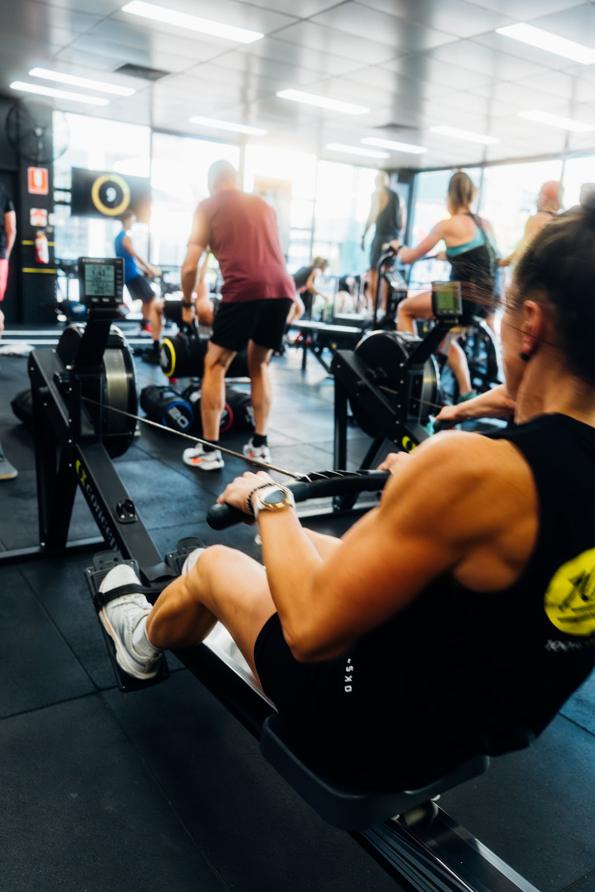 A group of people are engaged in a HIIT workout using rowing machines in a brightly lit gym.