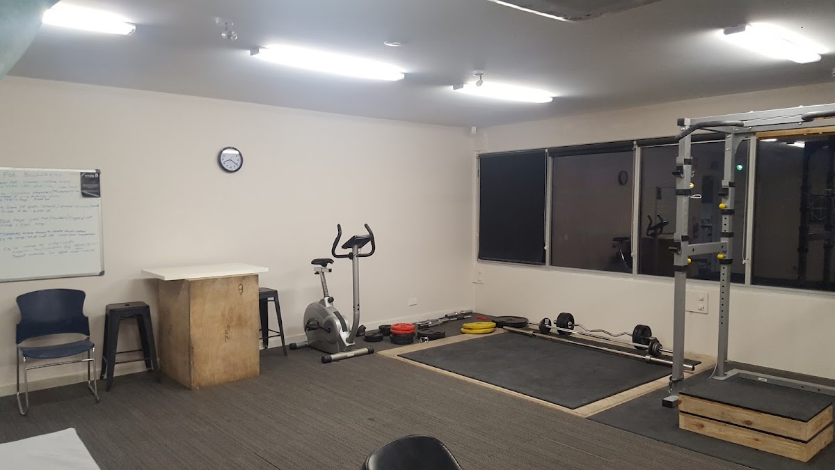 This photo shows a sparsely equipped gym space with weightlifting equipment and an elliptical machine.