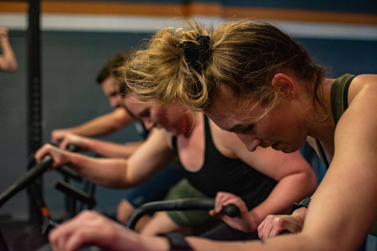 A group of people are intensely cycling on spin bikes in a brightly lit fitness studio.
