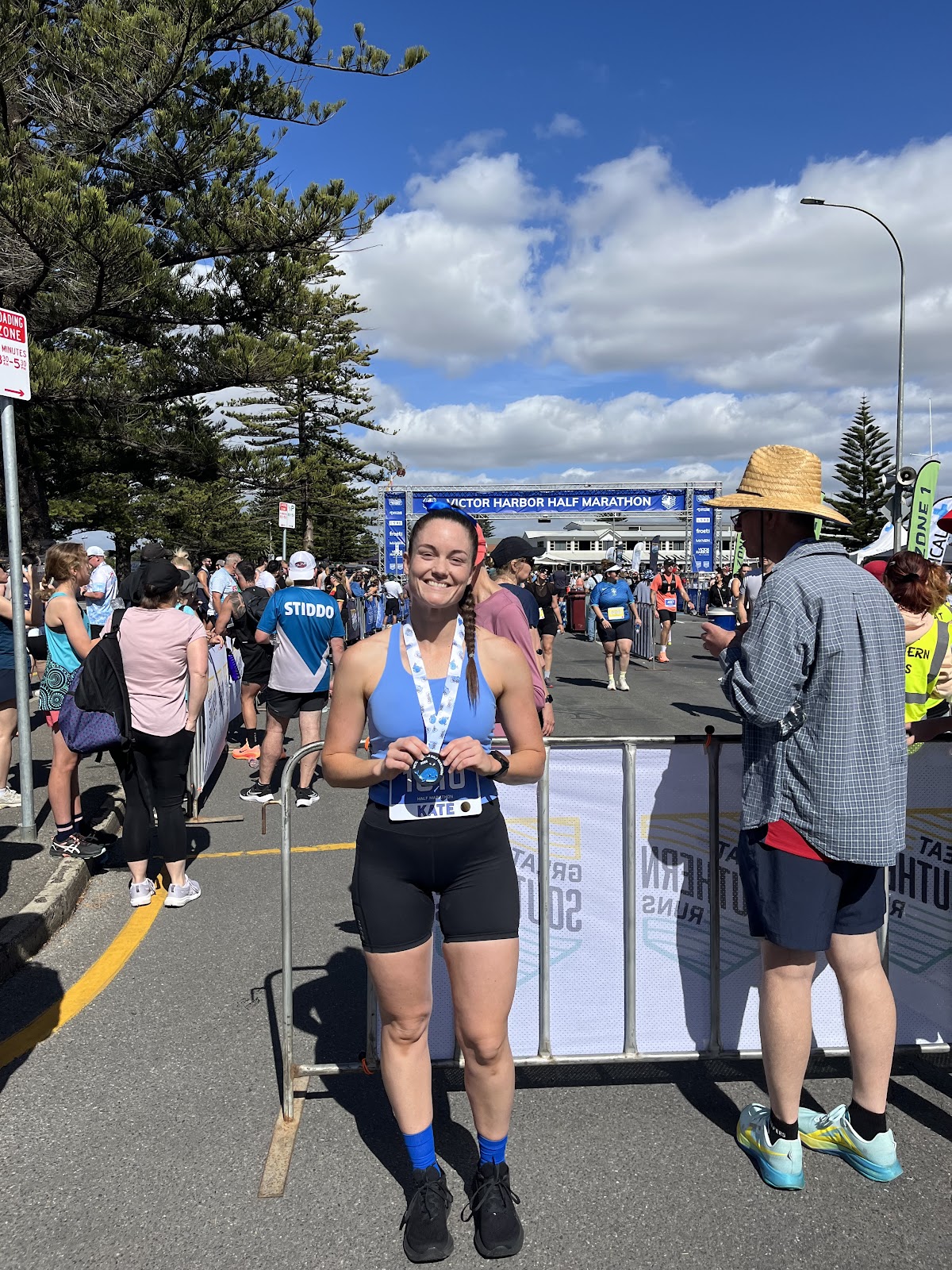 A runner proudly displays a medal after completing the Victor Harbor Half Marathon, surrounded by other participants and spectators.