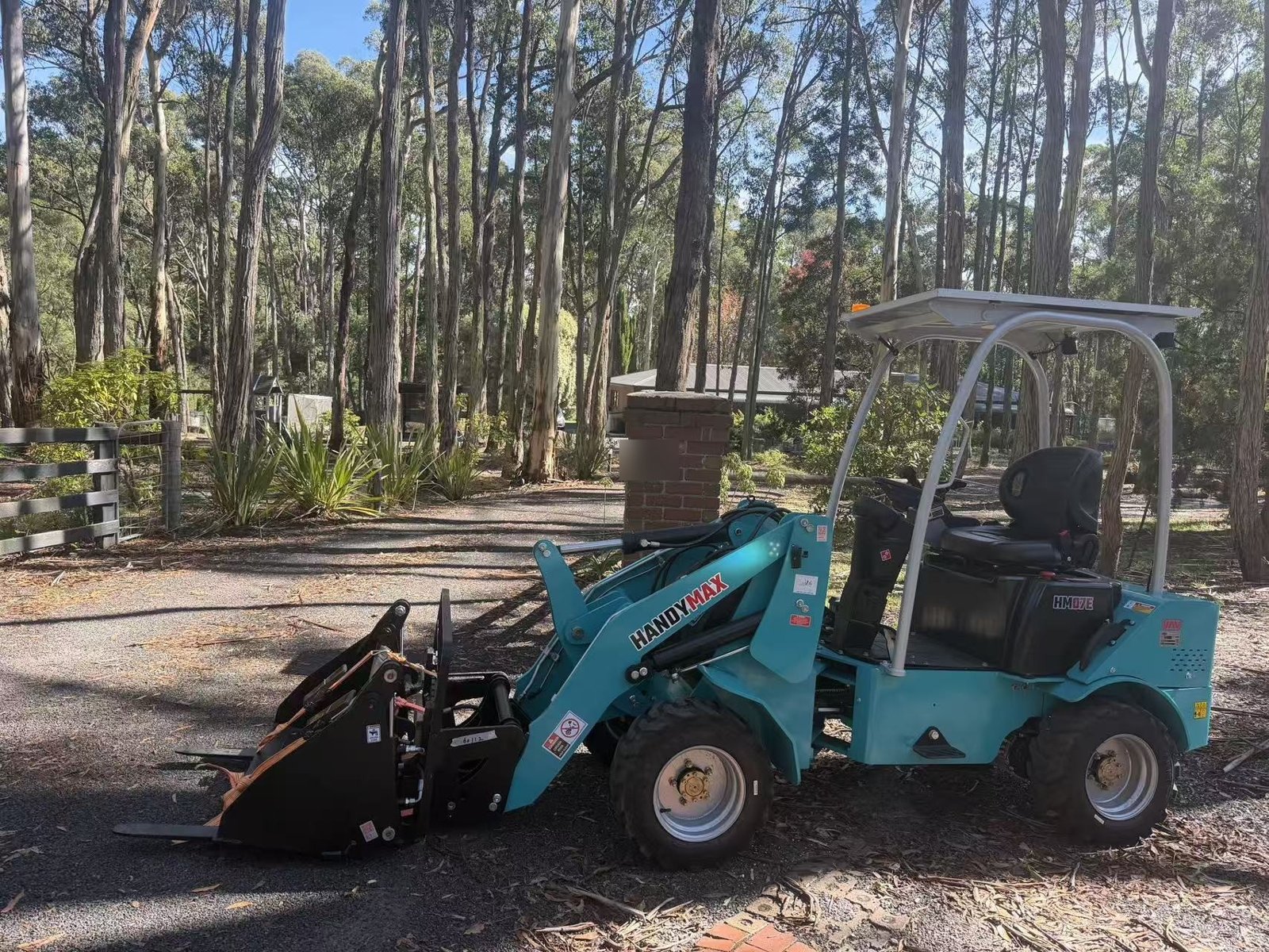 HandyMax HM07E electric wheel loader with a 4-in-1 bucket and pallet forks on a small property