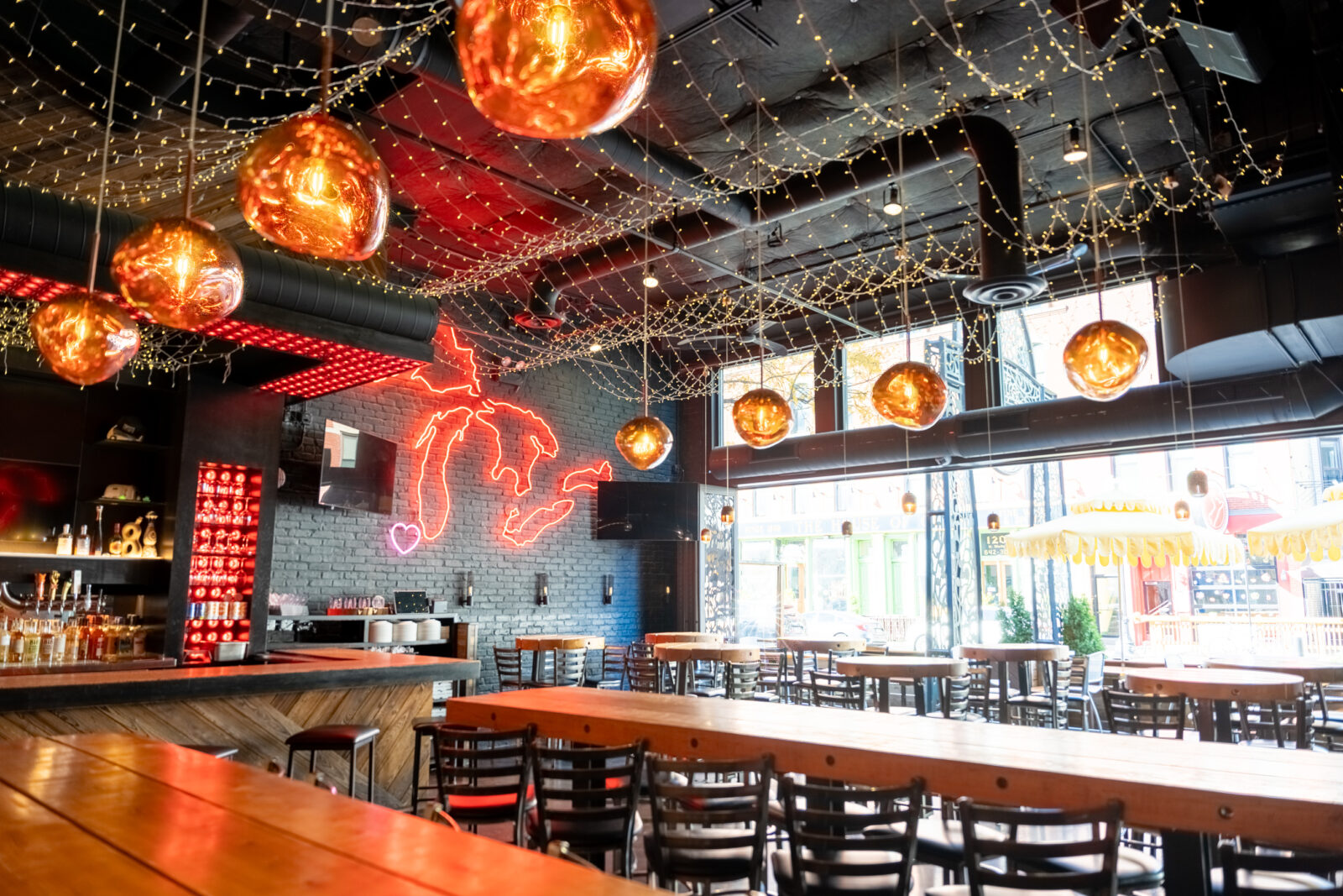 slide 1 of 3 - Open air indoor steaing with small and large long hightop tables. Large red neon sign of the great lakes