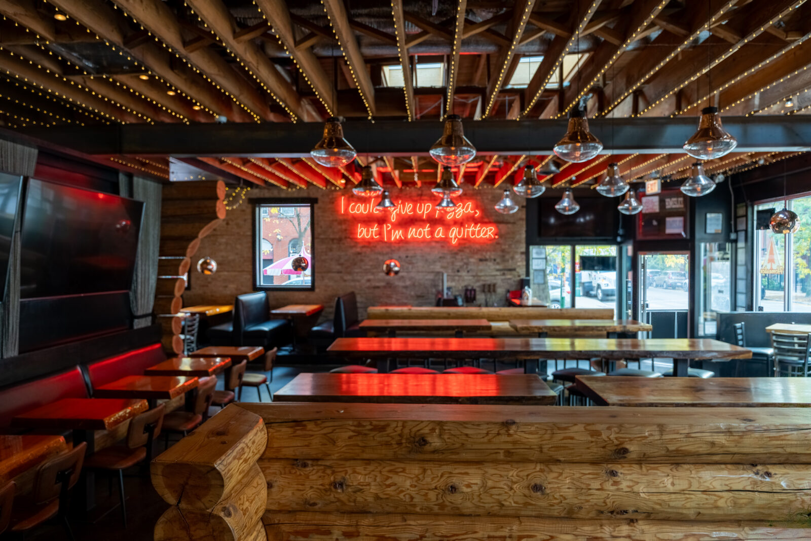 slide 2 of 5 - Inside log cabin style restaurant, high and low top booth seating, large red neon sign