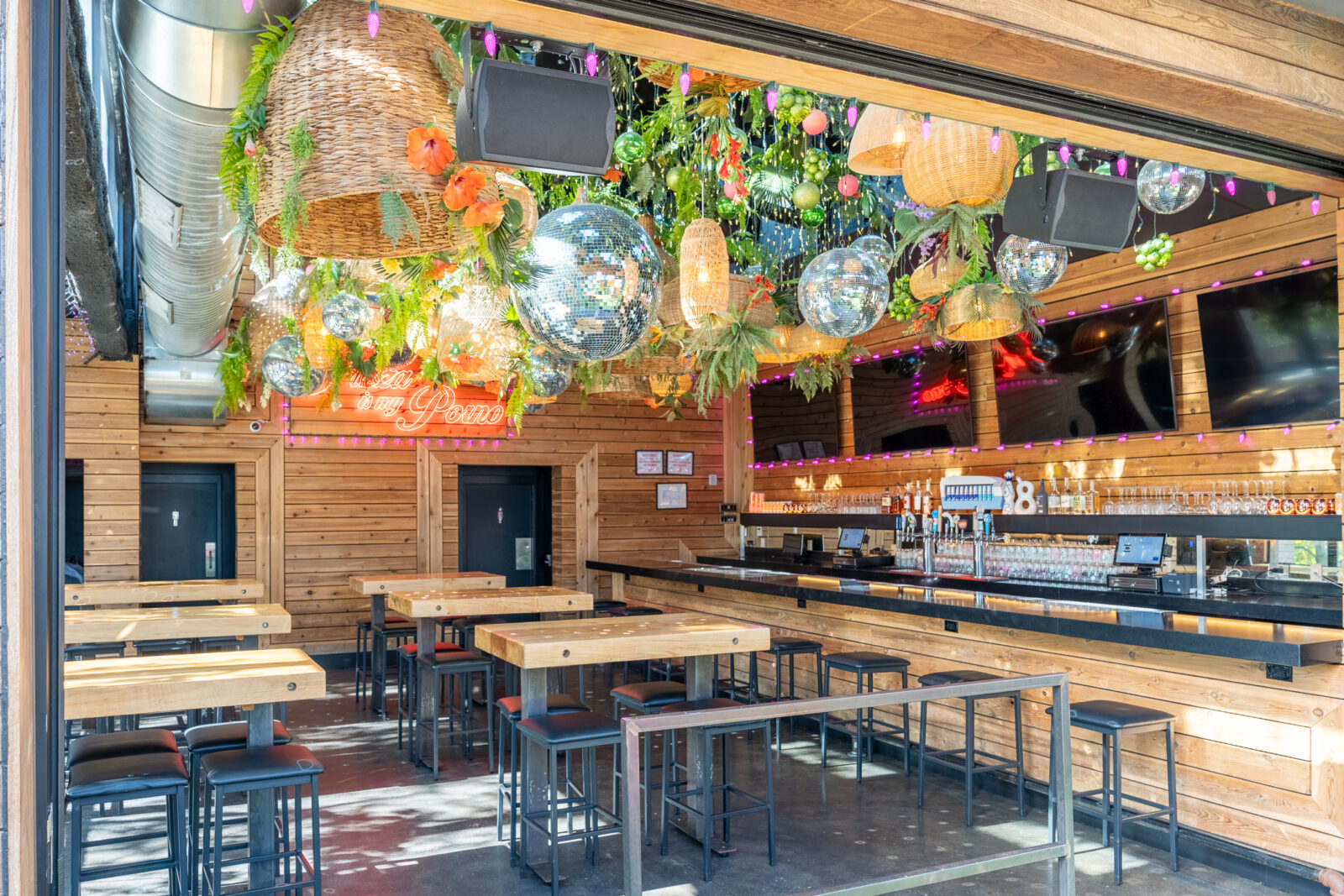slide 1 of 3 - Indoor bar area with long communal hightop seating, disco balls, grennery and tvs