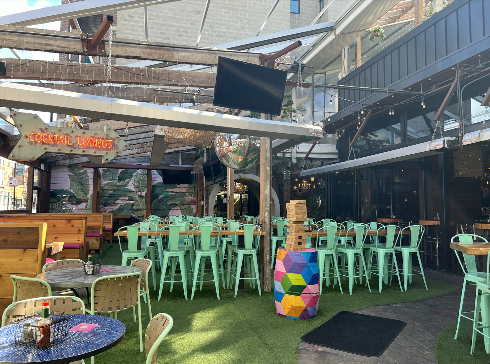 Front patio of paradise park. Cocktail lounge sign, disco balls and plants hanging above with all chairs and tables visible.