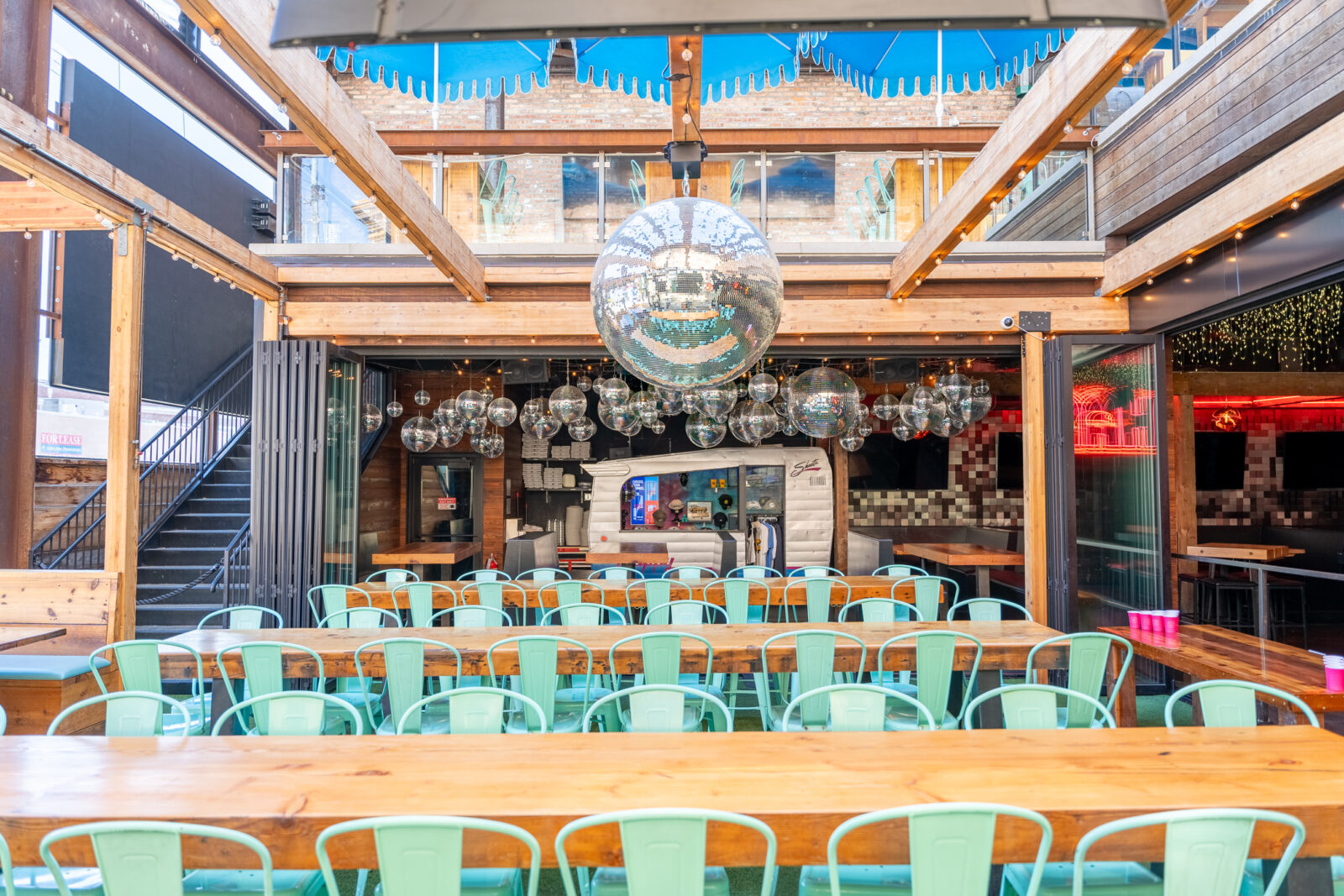 slide 2 of 2 - Open air patio, two floors, long communal hightop tables under large disco balls. clusters of small disco balls, small camper