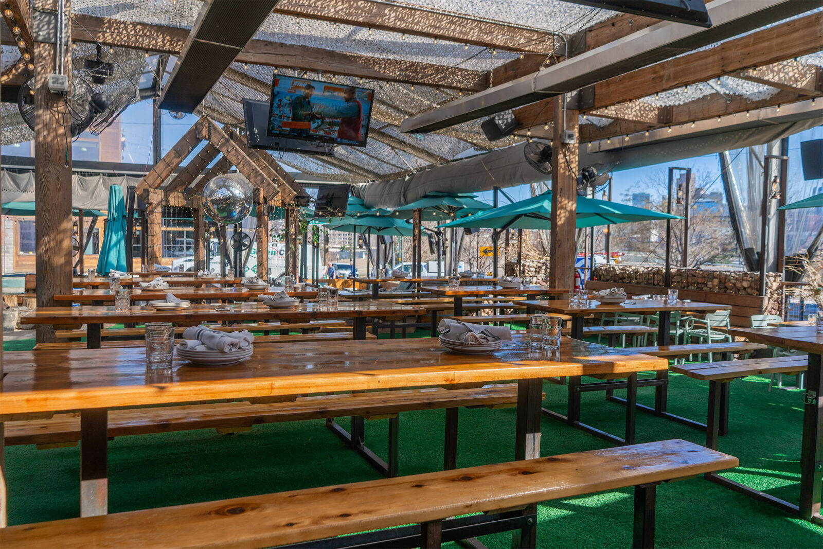slide 1 of 4 - Patio area, high top picnic style seating, blue umbrellas and tvs