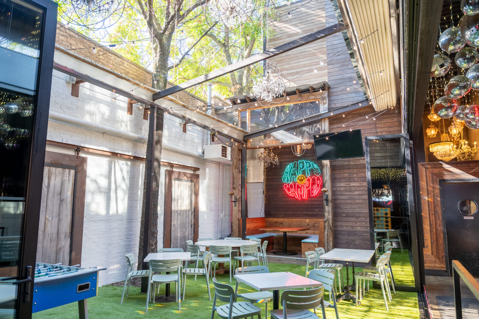 slide 1 of 1 - Outdoor beer garden with low top tables, and happy camper neon