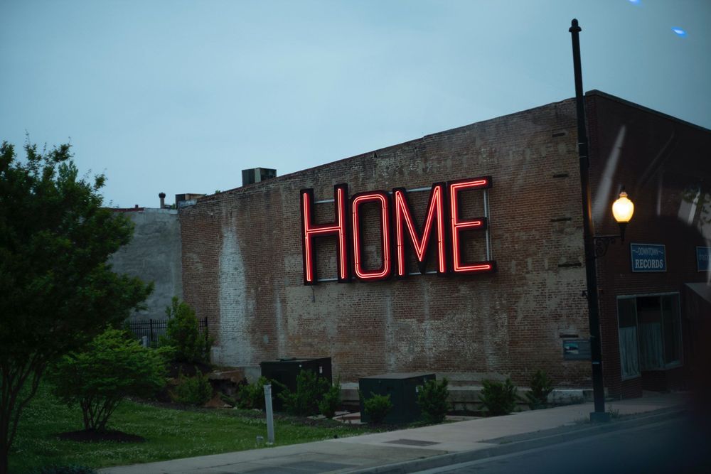 Brick building with a red neon "HOME" sign on it.