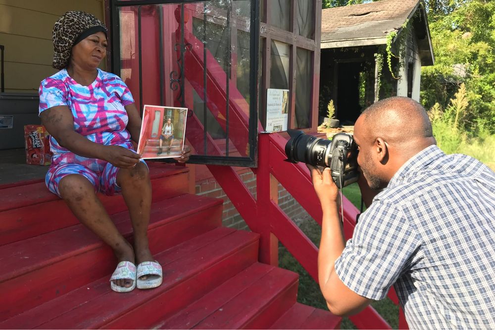 Man photographing a woman who is sitting on a set of steps holding a photograph