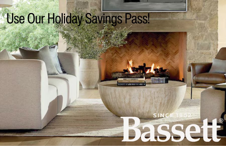 Contemporary living room scene with a beige square-arm sofa, a large round stone coffee table, and a stone fireplace. The decor includes an abstract painting and a tall vase with greenery.