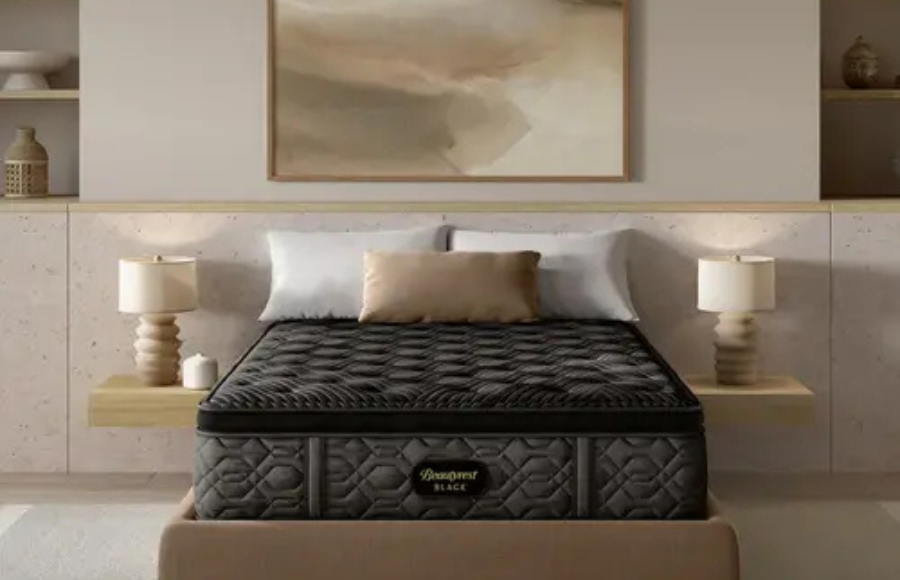 Contemporary living room scene with a beige square-arm sofa, a large round stone coffee table, and a stone fireplace. The decor includes an abstract painting and a tall vase with greenery.