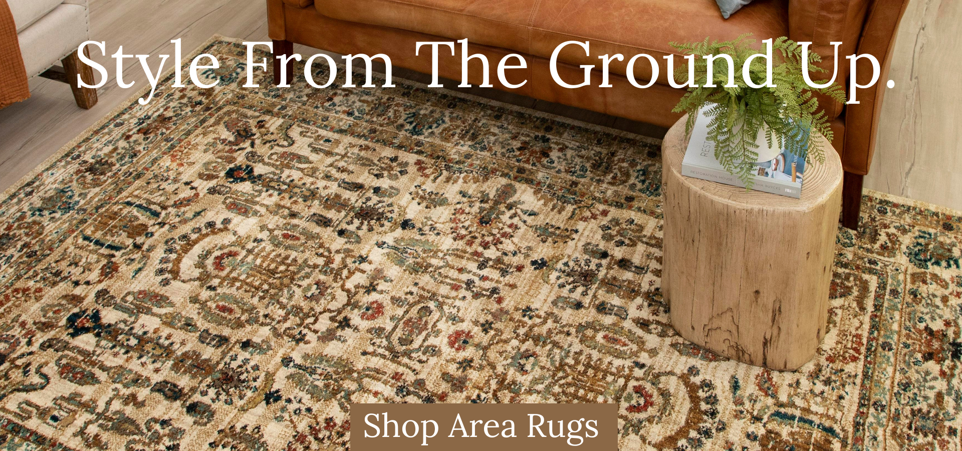 Earth-toned rectangular braided area rug with a concentric gradient pattern in a rustic living room setting featuring a wooden coffee table and tan sofa.