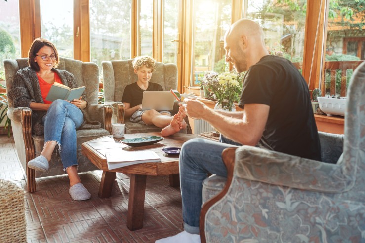 A family of three sits on armchairs inside a sunroom with each other, spending much-needed time together after a long day.