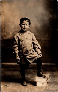 RPPC Boy in jacket short and hat stepping on books Badger