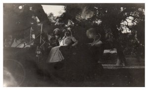Three people pose in an old car RPPC Postcard