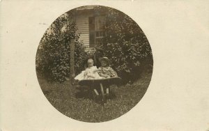 RPPC Postcard Vignette 2 Baby Toddler in Wheel Barrow Shadowy Man Stands Behind