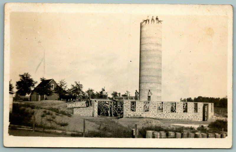 RPPC~Trio of Men Sit Atop Water Tower~Construction of Stone Plant Below~c1916 PC 