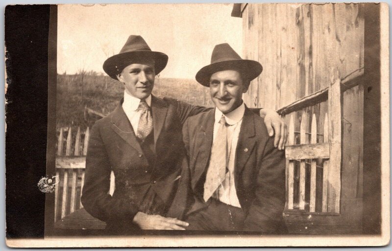 Two Men Photograph Suits Black Hats Fence & Barn Background RPPC Postcard 