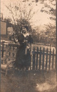 Woman in Black Dress Ribbon in Front of Fence Wicker Chair Portrait RPPC PC