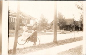 Two Young Ladies Bicycle on Residential Street Women Porch Sitting Postcard Y17