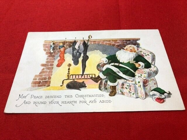 1928 embossed postcard SANTA Green Robe black cat relaxing by fire, hat on floor