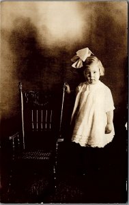 c1910 YOUNG GIRL BOW IN HAIR BESIDE ROCKING CHAIR REAL PHOTO RPPC POSTCARD 38-23