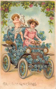 L302 Christmas Greetings Lady driving floral car Cupid Shamroc embossed postcard