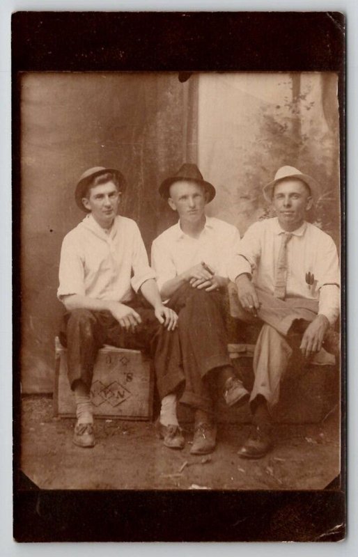 RPPC Three Men on Crates Dirt Floor Studio Prop Backdrop Hat Cigars Postcard F30