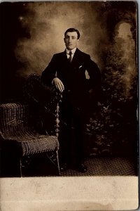 c1910 YOUNG GENTLEMAN IN SUIT AND TIE WICKER CHAIR AZO RPPC POSTCARD 38-48