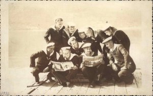Foreign Sailors on Dock Reading Magazines Ship Names Visible on Caps RPPC