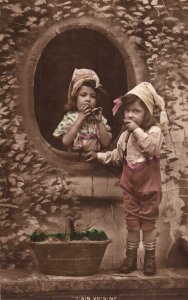 VINTAGE POSTCARD COUPLE OF CHILDREN WITH POMPOM HATS AND OVAL WINDOW POSTED 1915