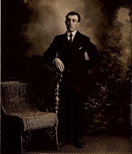 c1910 YOUNG GENTLEMAN IN SUIT AND TIE WICKER CHAIR AZO RPPC POSTCARD 38-63