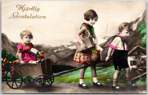 Hearty Congratulations Kida Pulling Cart Baby Riding With Flowers Postcard