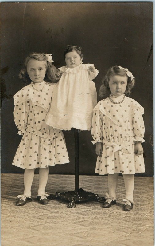 RPPC THREE SISTERS BABY ON POLE MATCHING DRESSES STERN FACES REALPHOTO POSTCARD