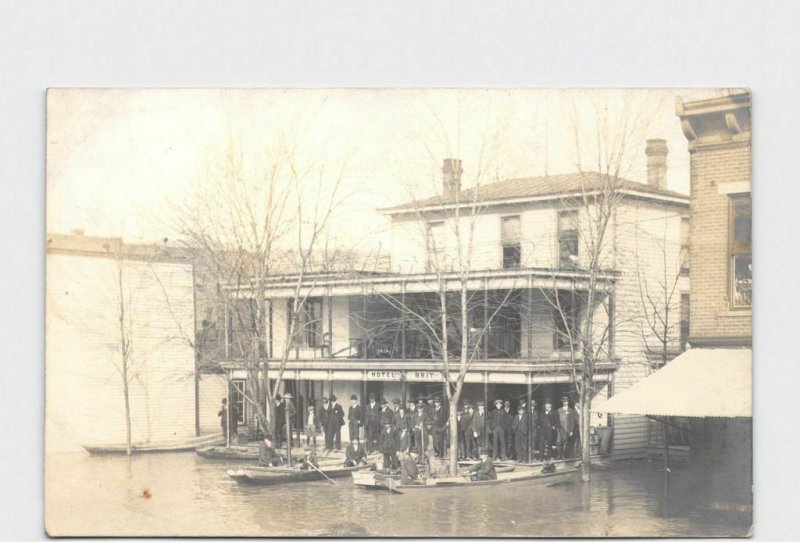 RPPC REAL PHOTO POSTCARD FLOOD MEN GATHERED ON PORCH OF HOTEL BRIT BOATS DOCKED 