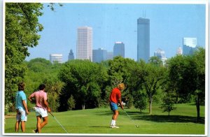 M-81003 The skyline of Minneapolis looms over these golfers at Theodore Wirth...