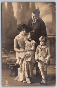 German Family of Four~Little Boy Holds Tennis Racket~Girl on Mom's Lap~RPPC 1910