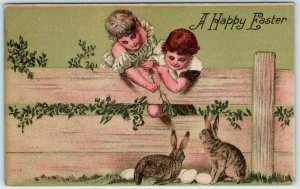 A HAPPY EASTER  Children Reaching Over Fence, Bunnies, Eggs ca 1910s Postcard